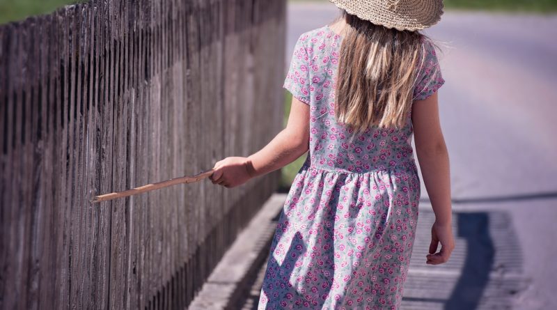 Girl touching wood fence with wood stick